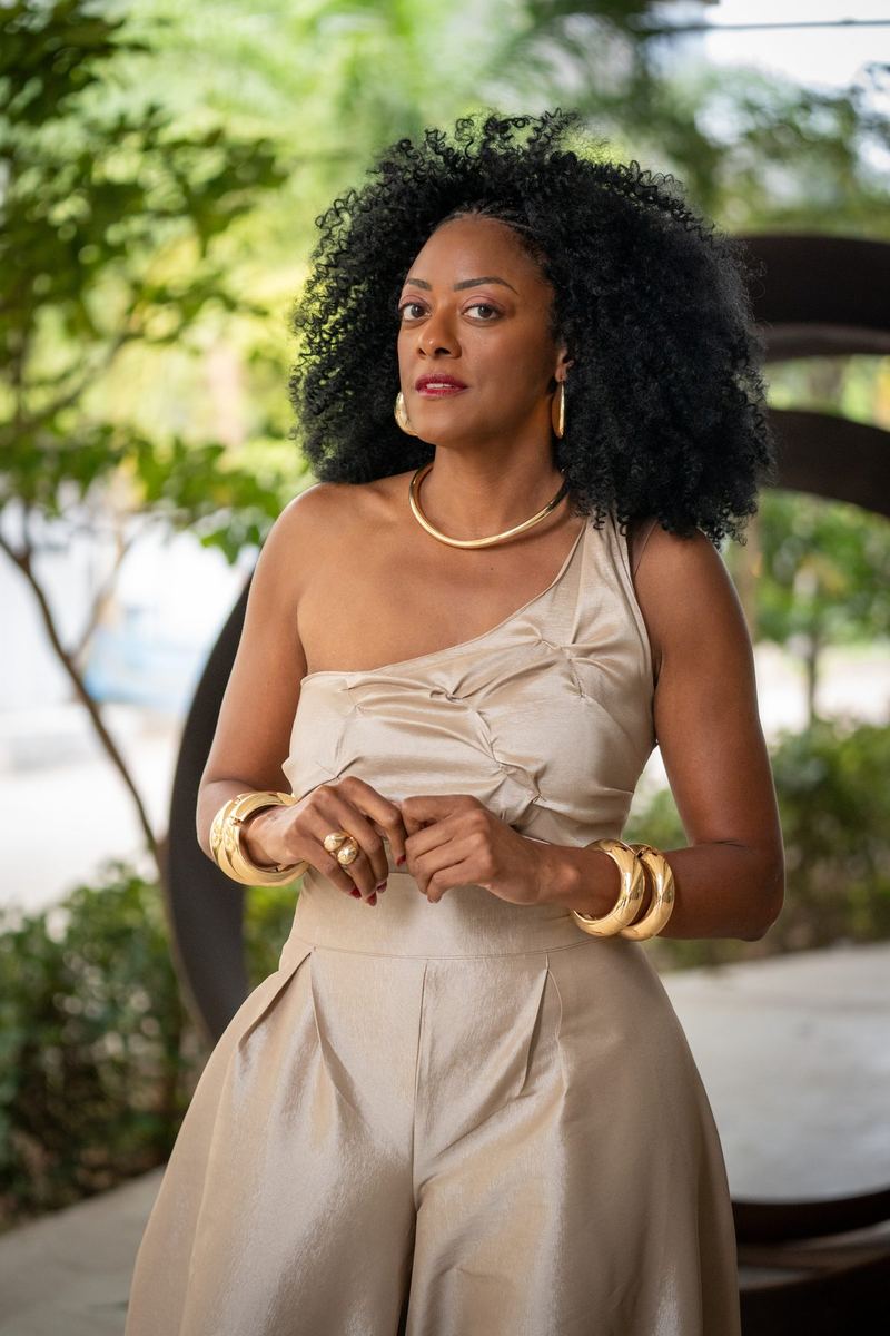 Retrato ao ar livre de mulher de cabelo cacheado volumoso e macacão dourado