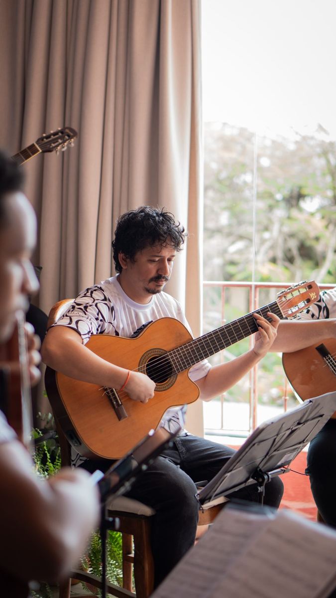 Músico tocando violão em sessão acústica ao lado de uma cortina