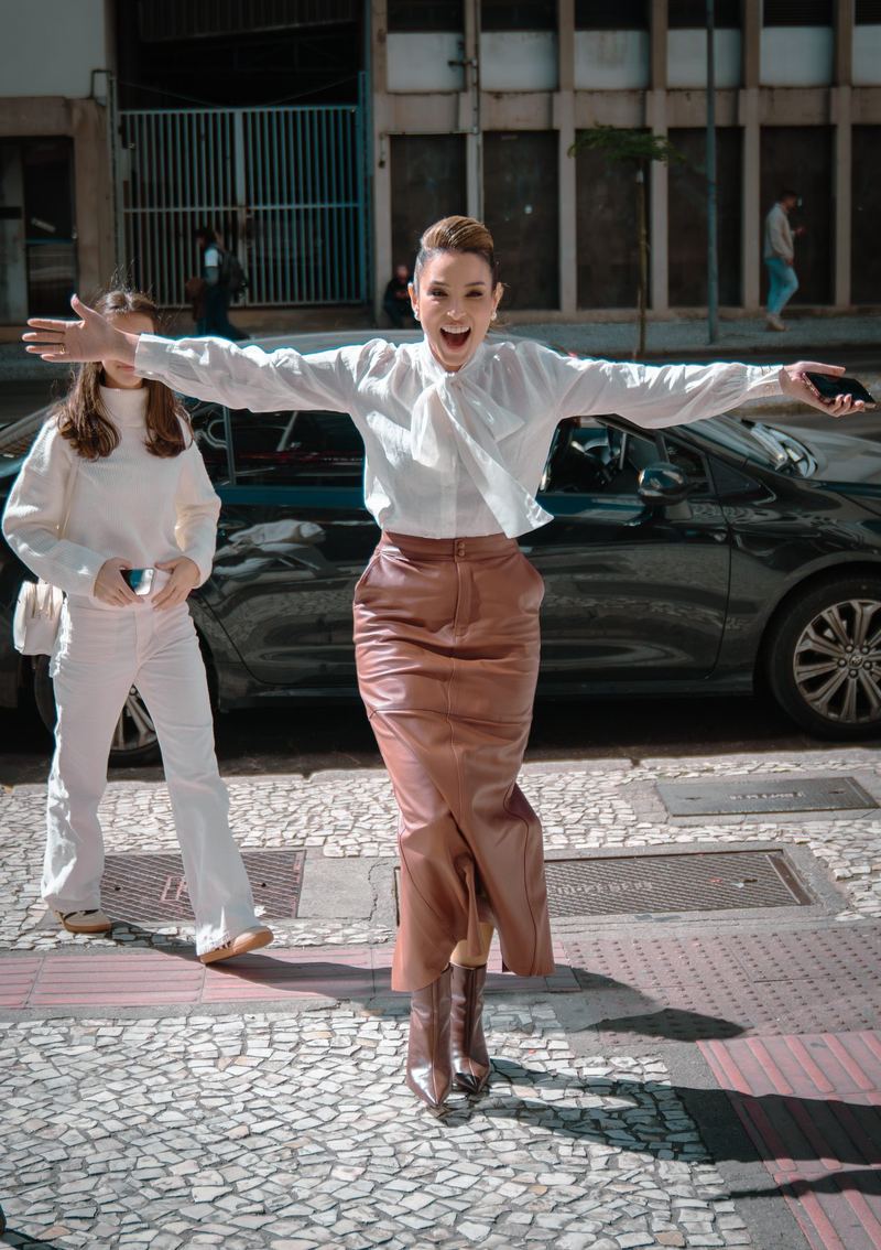 Mulher de braços abertos, rindo, em calçada da cidade