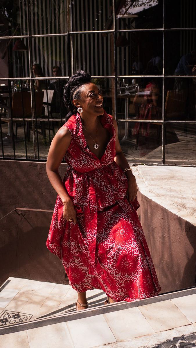Mulher de vestido vermelho estampado sorrindo ao subir uma escada sob luz dura