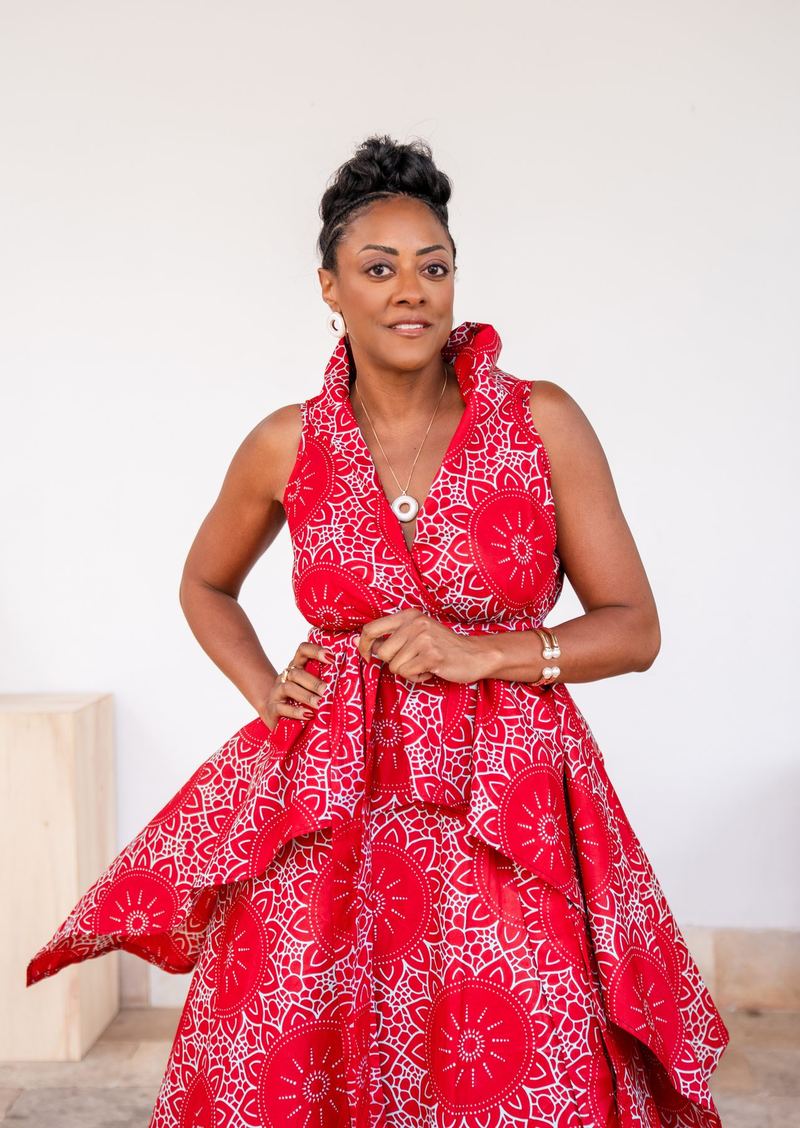 Mulher de vestido vermelho estampado posando diante de parede clara