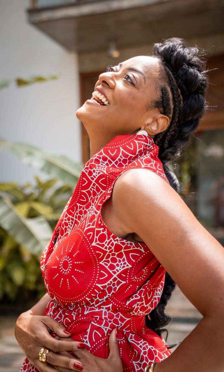 Mulher de vestido vermelho olhando para cima e sorrindo em pátio com plantas