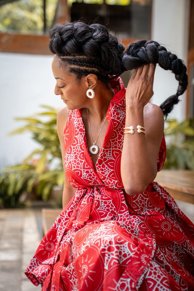 Mulher de vestido vermelho ajeitando a trança do penteado em pátio externo
