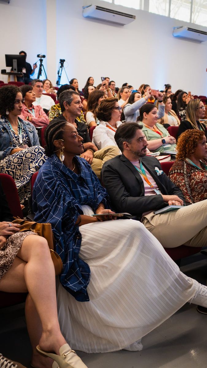 Plateia atenta durante palestra, com câmeras ao fundo