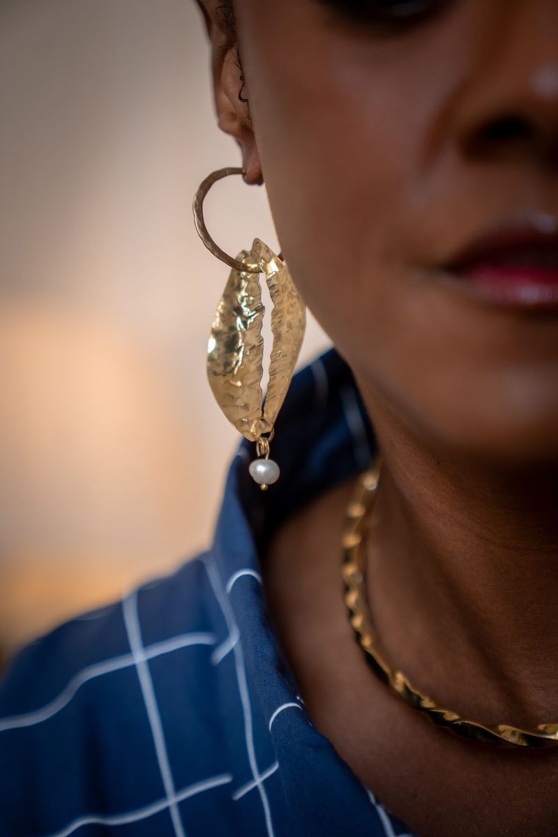 Detalhe de brinco dourado com pérola e colar, em close do rosto